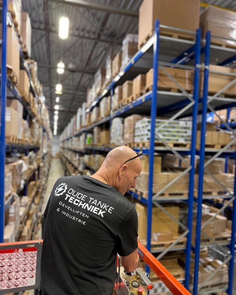 Monteur op een hoogwerker tussen magazijnstellingen