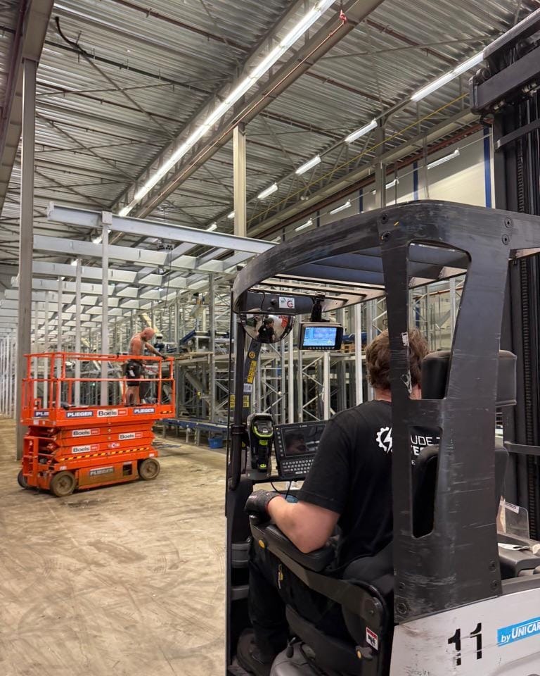 Monteur op een hoogwerker en een heftruckchauffeur tijdens de opbouw van een magazijninstallatie